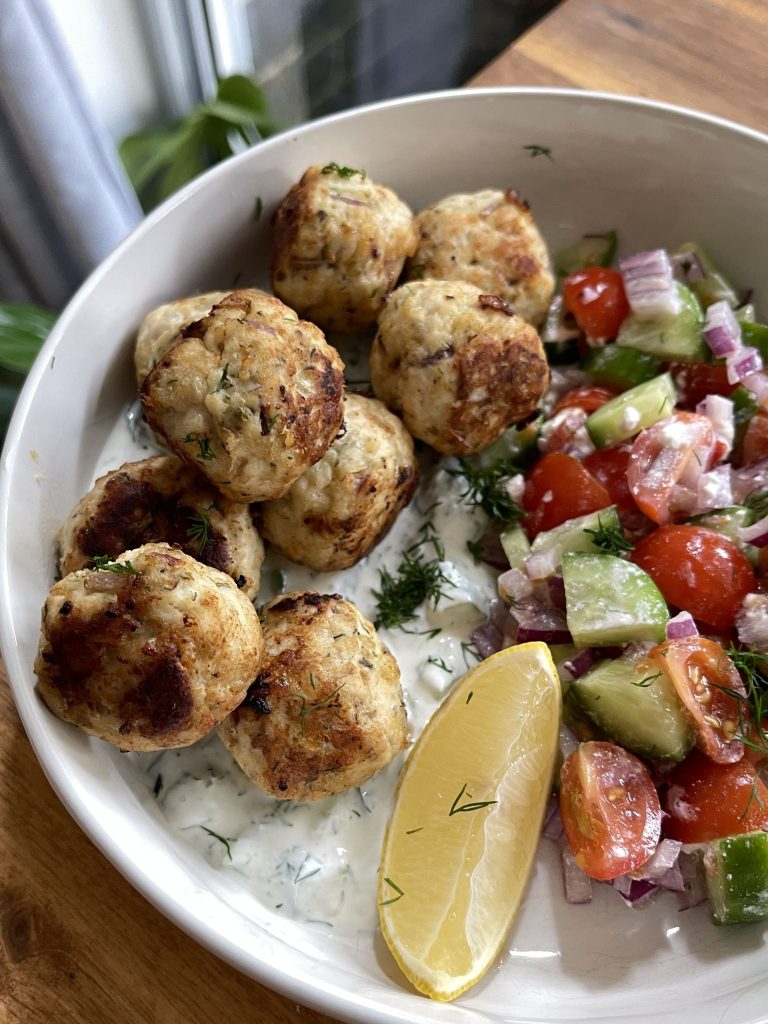 Close-up of golden-brown meatballs with creamy tzatziki sauce, garnished with dill