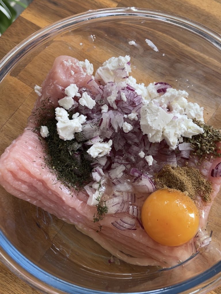 Ground turkey, panko, chopped red onion, feta, garlic, egg, and herbs combined in a mixing bowl, ready to form meatballs