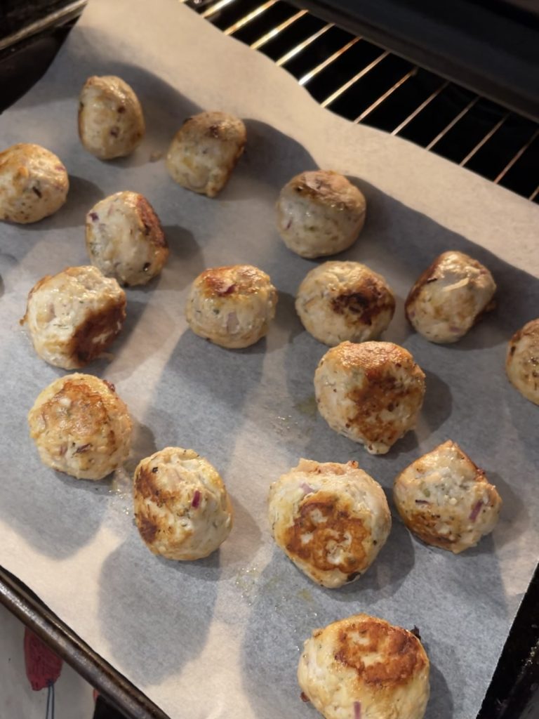 Meatballs baking on a lined tray at 200°C, finishing until golden and cooked through