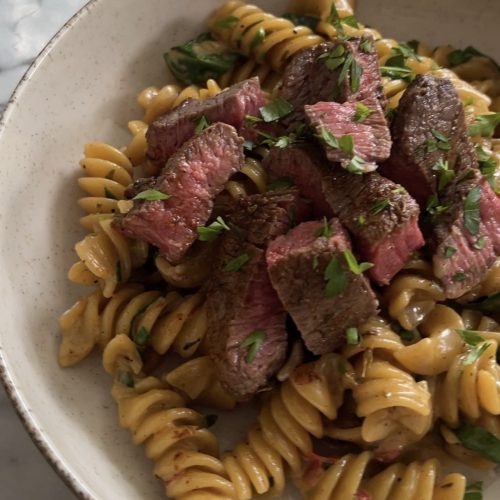 Creamy cajun pasta with sliced steak on top, garnished with parsley in a white bowl