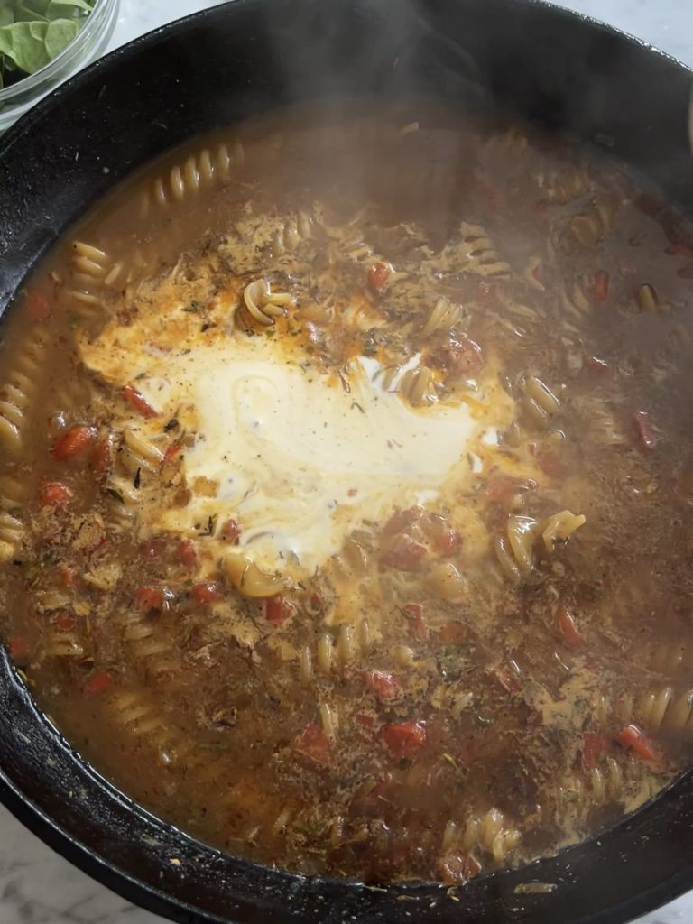 Pasta simmering in beef stock in the same pan, creamy sauce starting to thicken