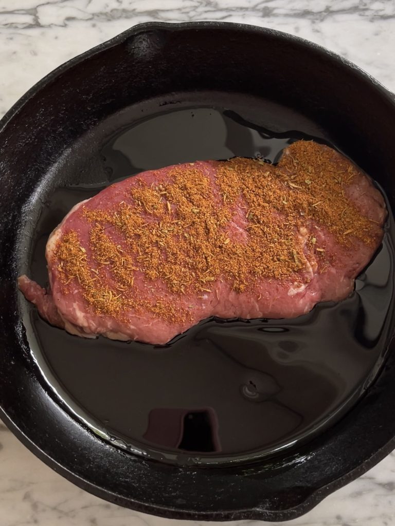 Seasoned steak in a black pan ready for searing