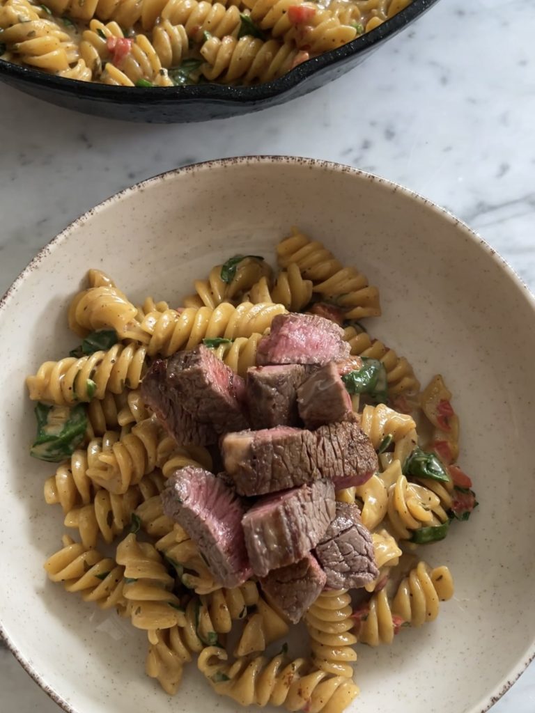 Sliced steak on creamy cajun pasta, served in a bowl with fresh parsley on top